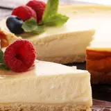 Una deliciosa tarta de queso, con una porción servida en un tenedor, decorada con frambuesas frescas y hojas de menta.