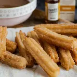 Montón de churros caseros recién hechos, espolvoreados con azúcar y canela, listos para mojar en chocolate caliente.