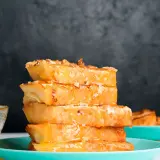 Torrijas de horchata doradas y jugosas, apiladas y bañadas en miel, con un cuenco de miel al lado.