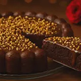 Deliciosa tarta de chocolate cubierta de glaseado y frutos secos. Una porción se sirve en una pala, con dos rosas rojas al fondo.