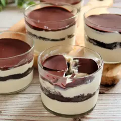 Cuatro vasitos de tiramisú de oreo, con capas de crema y galleta, cubiertos de chocolate.