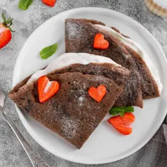 Deliciosos crepes de chocolate rellenos de crema, decorados con fresas en forma de corazón y espolvoreados con azúcar glas.