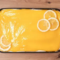 Un delicioso tiramisú de limón, cubierto con una crema amarilla brillante y decorado con rodajas de limón fresco.