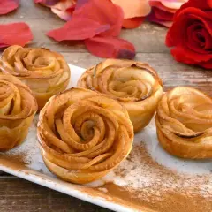 Deliciosas rosas de manzana horneadas, espolvoreadas con canela, junto a pétalos rojos y una rosa natural.