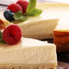 Una deliciosa tarta de queso, con una porción servida en un tenedor, decorada con frambuesas frescas y hojas de menta.