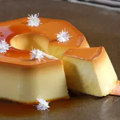 Delicioso flan de manzana con caramelo líquido y decorado con flores blancas. Una porción se sirve con una cuchara.