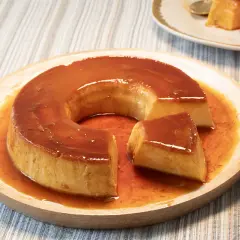 Un delicioso flan de leche condensada bañado en caramelo líquido, servido en un plato de madera.