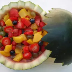 Deliciosa macedonia de frutas servida en una sandía tallada, con fresas, melocotón, uvas y arándanos.