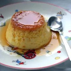 Delicioso flan de huevo casero con caramelo líquido, servido en un plato con dibujos infantiles.