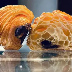 Dos mitades de un croissant de chocolate, una entera y otra cortada, revelan su interior aireado y el chocolate derretido.