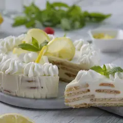 Deliciosa tarta de limón con leche condensada, decorada con crema batida, rodajas de limón y menta. Una rebanada muestra sus capas de galleta y crema.