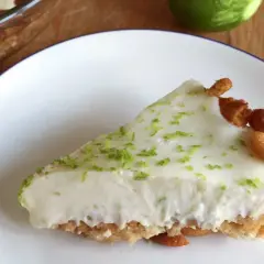 Rebanada cremosa de key lime pie, con ralladura de lima y trozos de galleta en el borde.