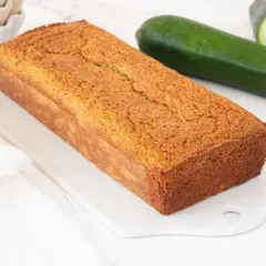 Bizcocho de calabacín dorado y esponjoso, listo para disfrutar. Dos calabacines frescos a su lado.