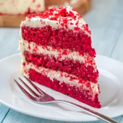 Rebanada de tarta red velvet con capas de bizcocho rojo y crema blanca, lista para disfrutar. Los ingredientes de esta tarta son un secreto delicioso.