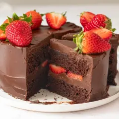 Deliciosa tarta de fresas y chocolate, cubierta de ganache y decorada con fresas frescas. Un trozo revela capas de bizcocho de chocolate y fresas.