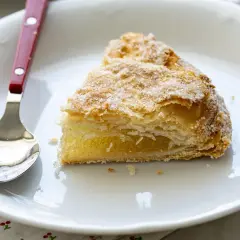 Un trozo de pastel cordobés, hojaldrado y cubierto de azúcar, espera ser disfrutado junto a una cuchara en un plato blanco.