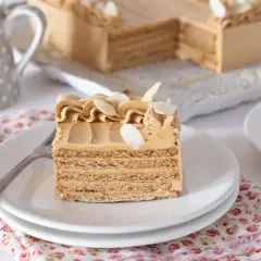 Deliciosa tarta de moka en capas, decorada con crema y almendras. Un trozo servido en plato blanco, listo para disfrutar.