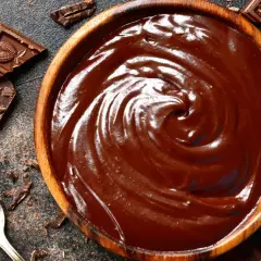 Un cuenco de madera lleno de cremoso de chocolate, con trozos de chocolate y virutas esparcidos alrededor.