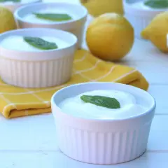 Delicioso mousse de limón mambo en ramequines blancos, adornado con hojas de menta. Limones frescos y una servilleta amarilla completan la escena.