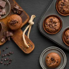 Deliciosos muffins de chocolate recién horneados, algunos en molde y otros listos para disfrutar, acompañados de trozos de chocolate y crema.