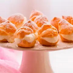 Deliciosos profiteroles de nata, espolvoreados con azúcar glas, listos para ser disfrutados en una bandeja blanca.