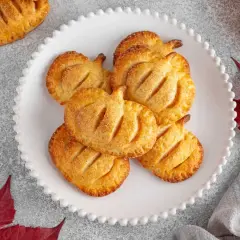 Deliciosos hojaldres de calabaza con forma de calabaza, espolvoreados con azúcar y canela, sobre un plato blanco festoneado.