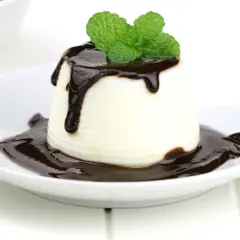 Deliciosa panna cotta de chocolate blanco, cubierta con salsa de chocolate y decorada con hojas de menta fresca.