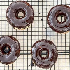 Cuatro deliciosos donuts glaseados con chocolate oscuro, listos para disfrutar. ¡Así es como hacer donuts caseros!