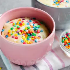 Un delicioso bizcocho al microondas en una taza rosa, cubierto de coloridas chispas. ¡Listo para disfrutar en minutos!
