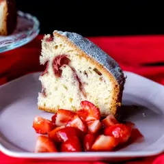 Rebanada de bizcocho de fresa esponjoso, espolvoreado con azúcar glas, servido con fresas frescas picadas en un plato rosa.