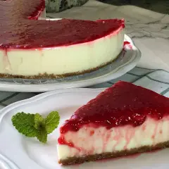 Deliciosa tarta de yogur sin horno cubierta con mermelada de frutos rojos. Un trozo servido con menta fresca.