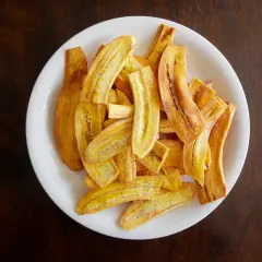 Un plato blanco lleno de crujientes rodajas de plátano frito, espolvoreadas con azúcar y canela.