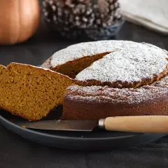 Dos rebanadas de bizcocho de calabaza apiladas, espolvoreadas con azúcar glas, con menta y tenedor.