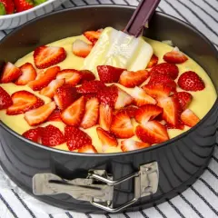 Bizcocho de yogur de fresa en molde, con fresas cortadas esparcidas sobre la masa y una espátula.