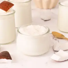 Delicioso mousse de coco en vasitos de cristal, decorado con coco rallado y trozos de coco fresco.