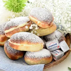 Bollos de mantequilla cubiertos de azúcar glas, rellenos de crema, junto a levadura y flores blancas.