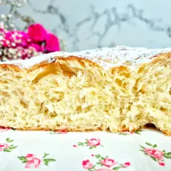 Una ensaimada mallorquina esponjosa, espolvoreada con azúcar glas, reposa sobre un mantel de flores.