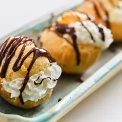 Profiteroles rellenos de crema y bañados en chocolate, perfectos para tu próxima receta.