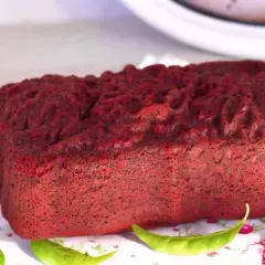 Un delicioso pan de red velvet, con una textura esponjosa y un color vibrante, decorado con hojas verdes sobre un mantel floral.