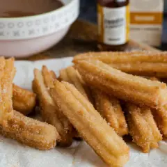 Montón de churros caseros recién hechos, espolvoreados con azúcar y canela, listos para mojar en chocolate caliente.