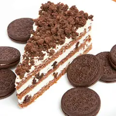 Rebanada de bizcocho de oreo con capas de crema y galleta triturada, rodeada de galletas oreo enteras en un plato blanco.