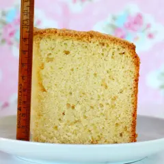 Rebanada de bizcocho de vainilla esponjoso, medido con una regla de madera. Fondo rosa con flores.