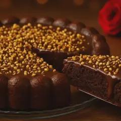 Deliciosa tarta de chocolate cubierta de glaseado y frutos secos. Una porción se sirve en una pala, con dos rosas rojas al fondo.