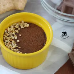 Pudín de chocolate cremoso en un cuenco amarillo, espolvoreado con cacao y nueces picadas.