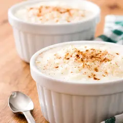 Dos ramequines de arroz con leche en microondas, espolvoreados con canela, sobre una mesa de madera.