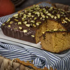 Bizcocho con harina de espelta, cubierto de chocolate y pistachos. Una rebanada muestra su interior esponjoso.
