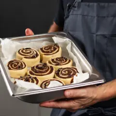 Manos sostienen una bandeja con deliciosos rollitos de canela listos para hornear.