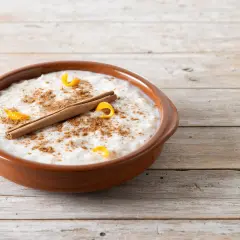 Un tazón de arroz con leche cremoso, espolvoreado con canela y adornado con cáscara de naranja y una rama de canela. ¡Perfecto para tu receta de arroz con leche cremoso!