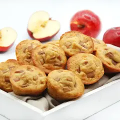Deliciosas magdalenas de manzana, recién horneadas y listas para disfrutar. Dos manzanas rojas enteras y dos cortadas a la mitad acompañan esta tentación.