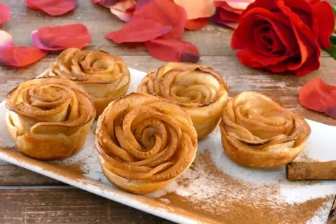 Deliciosas rosas de manzana horneadas, espolvoreadas con canela, junto a pétalos rojos y una rosa natural.
